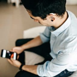 Younger man with a hearing aid using a smartphone.